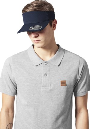Hallikas polo särk kahe nupuga ja pruuni ruudukujulise logoga plaastriga rinnas. Tumed sinine kübar. Sile kangastekstuuri.