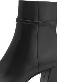 Bottine noire en cuir avec une fine bride et une boucle autour de la partie supérieure et un talon bloc.