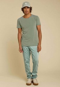 T-shirt en coton vert olive, pantalon vert menthe clair et chaussures beiges. La casquette assortie est vert olive avec un logo blanc. Coupe décontractée, texture lisse.