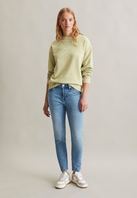 Lichtgroene sweatshirt met manchet-mouwen, gecombineerd met lichtblauwe slim-fit jeans en witte sneakers met beige accenten.