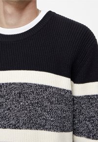 Pull rayé bleu marine et crème avec un motif en maille texturée, col rond et chemise blanche superposée visible.