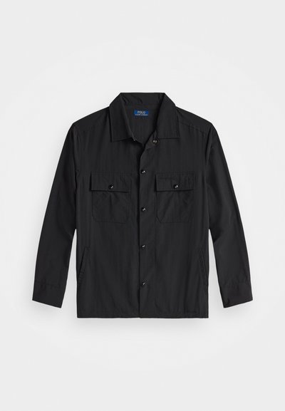 Μαύρο πουκάμισο με κουμπιά, κατασκευασμένο από ελαφρύ ύφασμα, με δύο τσέπες στο στήθος που κλείνουν με κουμπιά και απλό γιακά.