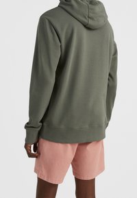 Felpa verde con cappuccio realizzata in tessuto morbido, abbinata a pantaloni corti rosa. Caratterizzata da maniche lunghe e polsini a coste, con una vestibilità comoda.