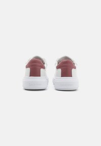 Sneakers bianchi con una tomaia in pelle liscia, dotati di un inserto sul tallone color bordeaux e suola di gomma bianca, con il marchio "Calvin Klein" sul retro.