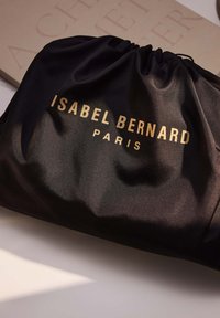 Schwarze Satin-Zugtasche mit goldener Schrift "ISABEL BERNARD PARIS." Glatte Textur mit gerafftem oberen Teil, minimalistisches Design.