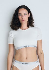 Haut court à manches courtes blanc et bas de bikini assorti avec une ceinture à logo Carhartt grise, texture lisse, design simple et forme ajustée.