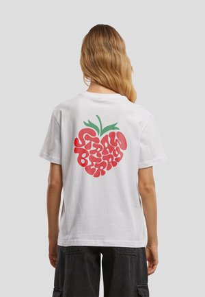 Person med langt hår iført en hvid t-shirt med et rødt og grønt jordbærmotiv og ordet "Strawberry" på ryggen.