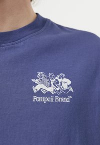 Camiseta de algodón azul marino con un gráfico blanco de tres figuras corriendo y el texto "Pompeii Brand" debajo, cuello redondo, textura suave.