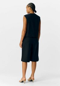 Zwarte mouwloze top gecombineerd met knielange shorts. Glad materiaal met een strakke silhoutte, met een eenvoudig ontwerp en neutrale tinten.