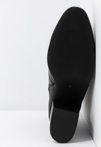 Zapato formal negro colocado con la suela hacia arriba sobre una superficie blanca, mostrando una suela suave con el número de talla "4" cerca del talón.