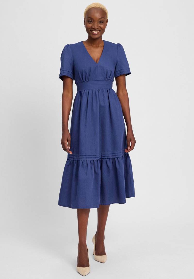 Marineblaues Kleid mit V-Ausschnitt und kurzen puffÄrmel. Das Kleid hat eine taillierte Taille und einen gestuften Rock mit horizontalen Nahtdetails.