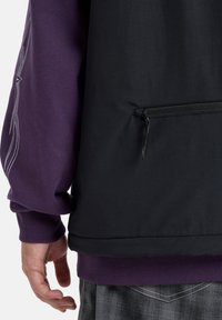 Abbigliamento a strati nero e viola con tasca con zip, polsini a costine e una texture di tessuto liscia con un motivo decorativo sulla manica.