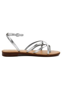 Sandali in pelle metallica argentata con più cinturini incrociati e cinturino alla caviglia. Suola piatta con soletta in pelle marrone chiaro e bordi texturizzati.