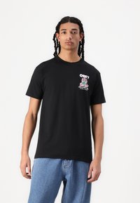 Svart bomull T-skjorte med korte ermer, med et frontgrafikk i rosa og grønn som leser "OBEY LOVE & UNITY." Klassisk rund hals.