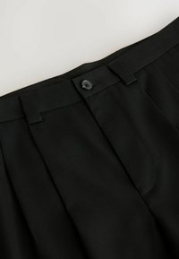 Sorte bukser med folder, der har en glat tekstur, en knaplukning og en slank talje. Stoffet ser velstruktureret og holdbart ud.