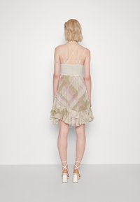 Kukkakuosisessa vaaleanvihreässä mekossa on röyhelöhiha, pitsireunuksellinen pukuosa ja ristikkäiset selkäremmit. Valkoiset sandaalit.