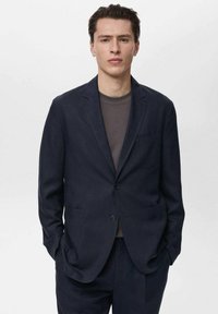 Blazer navy cu două buzunare frontale, cu rever în formă de U și închidere cu un singur nasture, purtat cu un tricou gri. Textură fină, design clasic.