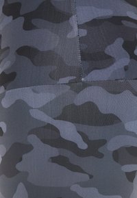 Černá a šedá maskáčová látka s hladkým texturem, obsahující různé odstíny šedé a výrazné tvary v přiléhavém designu.