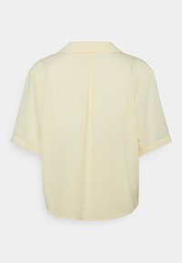 Vue arrière d'une chemise à manches courtes de couleur jaune pâle, en tissu lisse, dotée d'un col classique et d'un pli central.