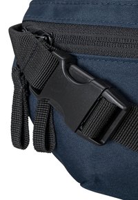 Borsa di tessuto blu navy con una tracolla nera regolabile, caratterizzata da una grande fibbia in plastica e dettagli di superficie texturizzati vicino alla cerniera.