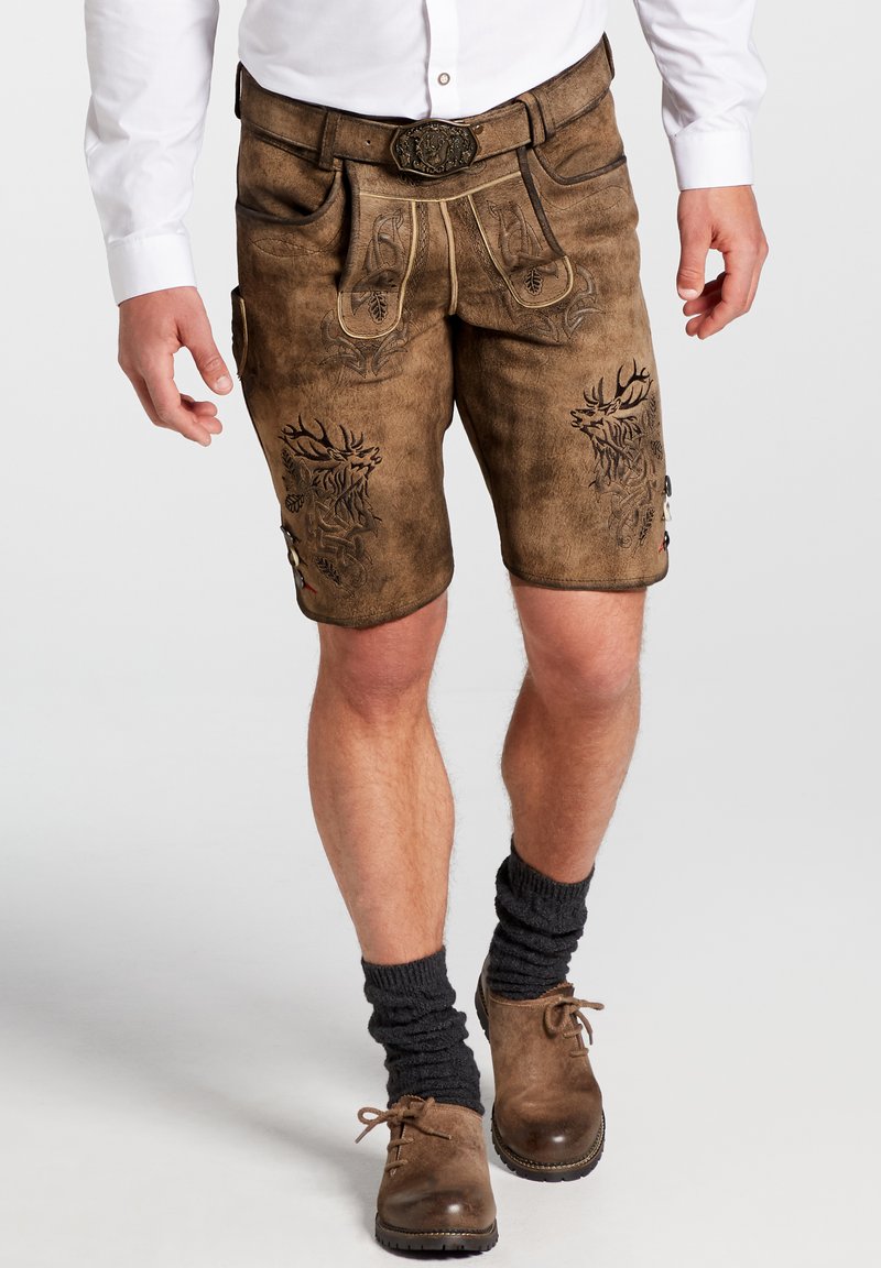 Pantalones cortos de cuero marrón con intrincados bordados, bolsillos laterales, herrajes decorativos, y combinados con calcetines oscuros y zapatos marrones.