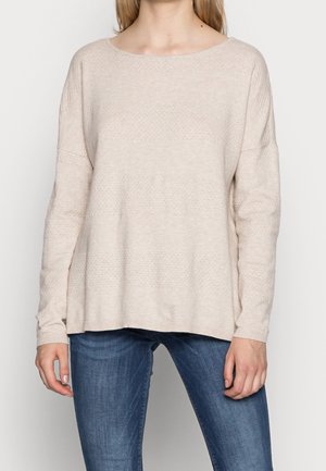 Maglione in maglia texturizzata color beige chiaro con un ampio scollo e spalle cadenti, dotato di maniche lunghe e una vestibilità rilassata. Abbinato a jeans blu.