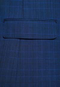 Granatowy materiał w kratę, z niebieskimi paskami. Zawiera kieszeń na piersi z klapką i teksturowane wykończenie tkaniny.