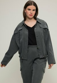 Szara, oversize kurtka z guzikami z przodu, kieszeniami na piersi i ściągaczem u dołu. Połączona ze spodniami w tym samym odcieniu szarości z kieszeniami po bokach.