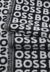Sort og grå tørklæde med gentaget "BOSS" mønster, lavet af blødt stof, med frynsede kanter og en struktureret vævning.