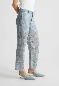 Pantaloni in pizzo azzurro chiaro con motivo floreale, dotati di una vita in pelle di jeans. Abbinati a tacchi a punta azzurro chiaro decorati con borchie.
