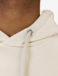 Krämfärgad hoodie med rund hals, prydd med en silverhål och en flätad dragsko. Tyget ser mjukt och texturerat ut.