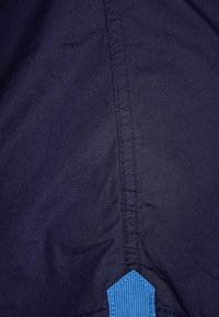 Tessuto blu navy con una trama liscia, caratterizzato da un accento testurizzato blu e cuciture a contrasto lungo la cucitura, creando un aspetto slanciato.