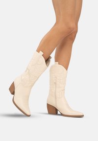 Botas de vaquero de imitación de cuero blancas con puntera afilada, detalles de costura y un tacón de bloque de altura media, con un cierre de cremallera lateral y una pestaña de agarre.