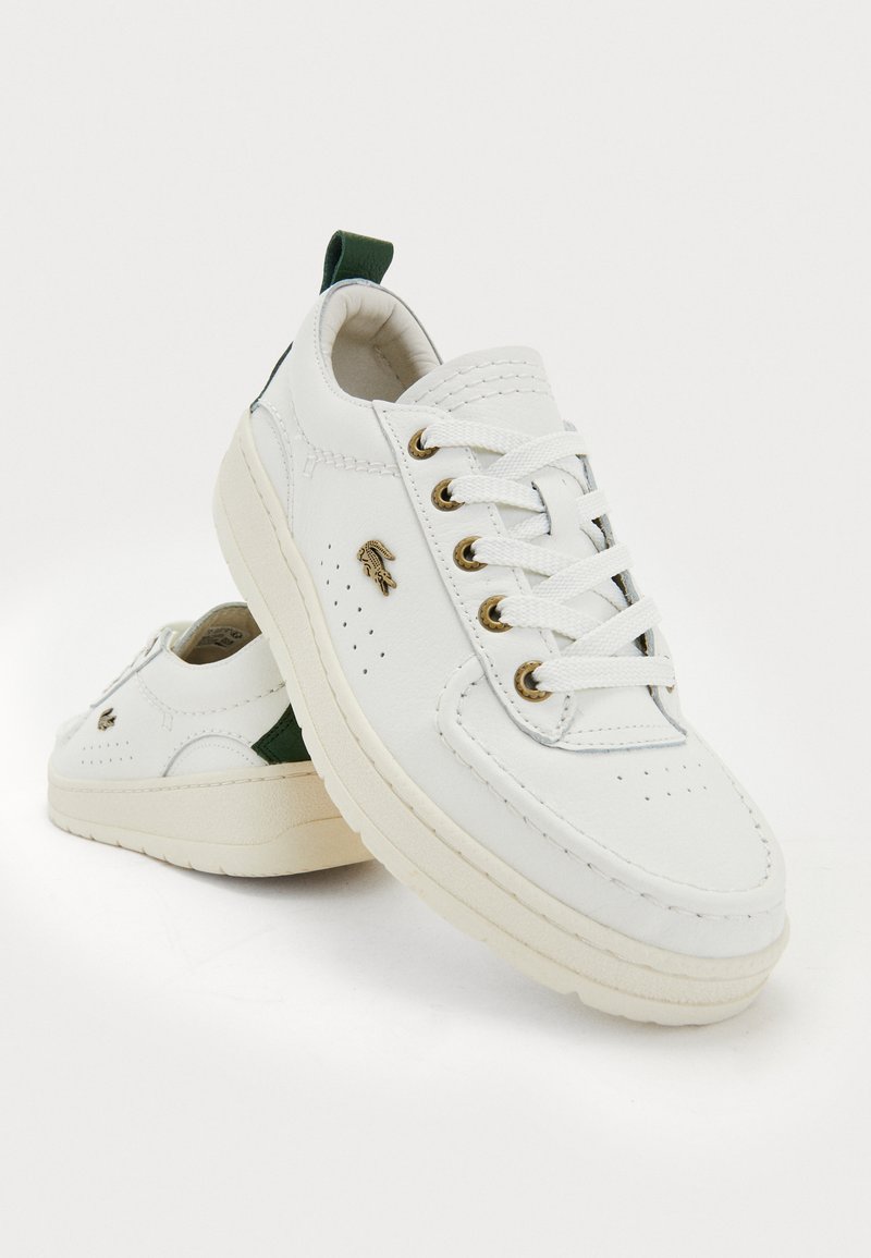 Baskets blanches en cuir avec des éléments en or, des accents verts et des détails perforés. Comprend une semelle texturée et des lacets plats.