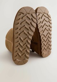 Brown suede ankle boots with textured rubber soles featuring a zigzag tread pattern. Zipper detail on the side for ease of wear.