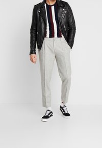 Sort læder bikerjakke over en stribet marineblå og bordeaux skjorte, kombineret med lysegrå plisserede bukser og sorte sneakers.