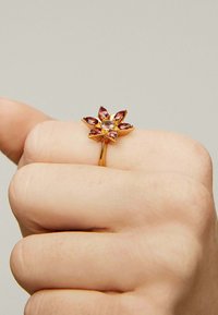 Anillo de oro con forma de estrella, adornado con gemas de corte marquesa en tono rosa y una gema redonda central. La textura es suave con acentos pulidos.