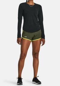 Långärmad svart träningsskjorta med texturerad tyg, kombinerad med olivgröna shorts med gula accenter och en logotyp. Svarta träningsskor.