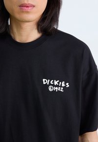 T-shirt en coton noir avec col rond, arborant le texte blanc "DICKIES" et le symbole de copyright, placés sur la zone gauche de la poitrine.