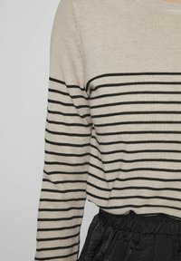 Długi rękaw, jasnobeżowy sweter w czarne poziome paski, zestawiony z czarną spódnicą z zaznaczoną talią. Styl jest casualowy i luźny.