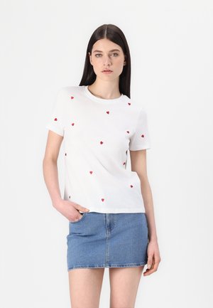 T-shirt en coton blanc à manches courtes, orné de petits appliqués en forme de cœurs rouges dispersés, associé à une mini-jupe en denim bleu.