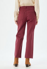 Jeans larghi bordeaux con orlo grezzo, design a cinque tasche e dettagli con yoke posteriore. Abbinati a stivaletti alla caviglia color sabbia.