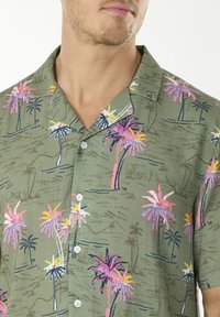 Camicetta a maniche corte realizzata in tessuto leggero, con una base verde e motivi di palme multicolori, e cinque bottoni sul davanti.