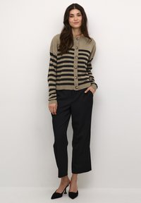 Kreemja ja musta triibuline kudumikaelus, millel on nööbid, kombineeritud mustade kohandatud pükste ja mustade kontsakingadega. Sile tekstuur, kitsas disain.