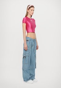 Rožinis atlasinis trumpas viršus su trumpomis rankovėmis; laisvi mėlyni džinsiniai cargo kelnės su daugybe kišenių ir laisvu kirpimu. Baltos sportbačiai.