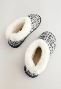 Black and white tweed slippers with soft white faux fur lining and sole. Rounded toe design, flat non-slip bottom for indoor use.