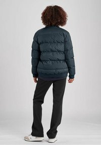 Mörkblå puffjacka med horisontella quiltade sektioner, ribbade manschetter och hög krage, dragen över svarta byxor och vita sneakers.