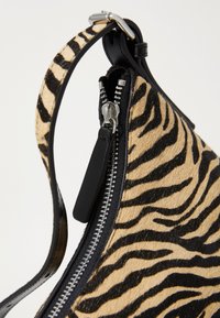 Black and tan zebra-print handbag with a smooth texture, metal zipper, and a black leather strap. Features a streamlined, curved design.
