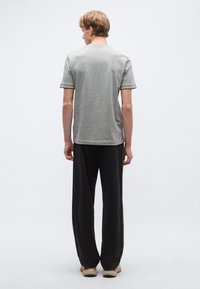 Szürke rövid ujjú ing strukturált felülettel és fekete, bővebb fazonú nadrág. Mindkét ruhadarabon kontrasztos szegély és semleges színpaletta található.