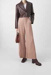 Veste croppée en cuir synthétique marron avec des accents texturés, associée à un pantalon large blush. Des bottines à talons carrés brillantes marron complètent le look.